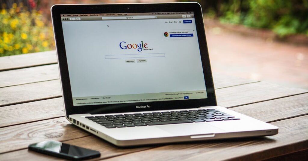 A MacBook Pro displaying Google Search on a wooden table outdoors, next to a smartphone.