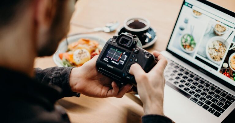 A man reviews photo settings on a camera while working on a laptop in a cozy workspace.