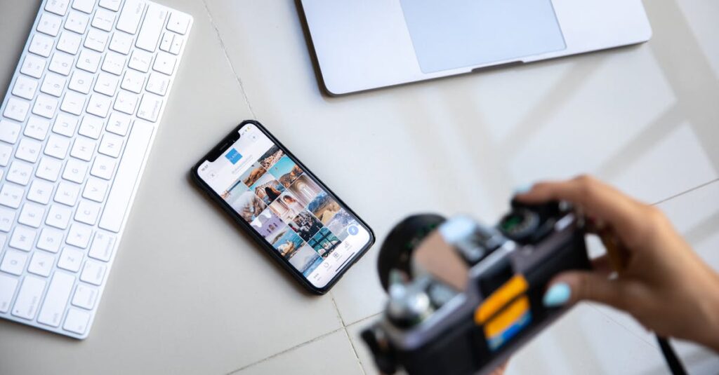 Person using vintage camera with smartphone and laptop in creative setup.