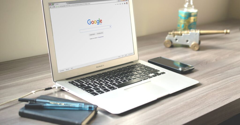 A neat workspace featuring a laptop displaying Google search, a smartphone, and a notebook on a wooden desk.